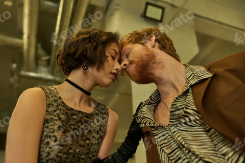 Preview: low angle view of stylish interracial couple kissing in public laundry in evening