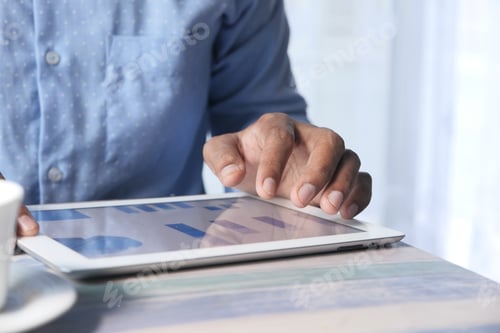 Preview: man's hand working on digital tablet at office desk, using self created chart