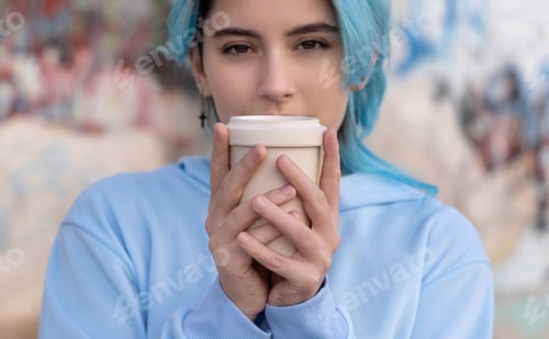 Preview: Blue haired Teenage girl in light blue oversize hoodie staying near graffiti wall with coffee to go