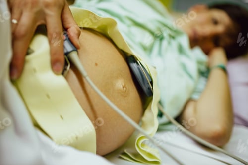 Preview: Pregnant woman lying in a hospital bed with baby heartbeat monitor on her belly