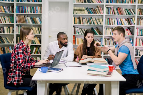 Preview: Group of friends groupmates, smart multiracial boys and girls, sitting in the library and helping