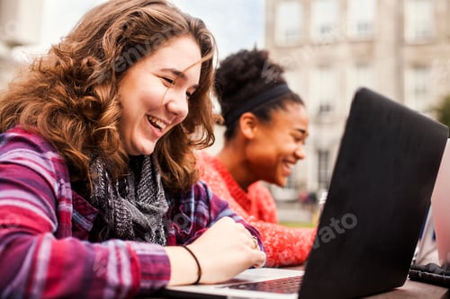 Preview: Happy female student using laptop with friend in background at campus
