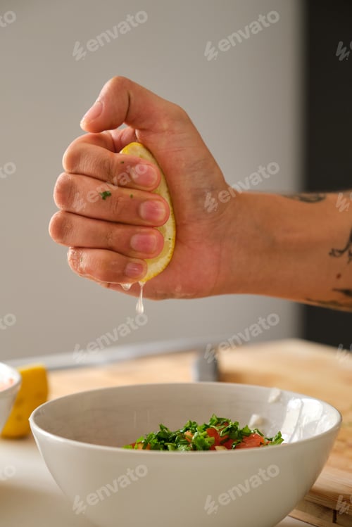 Preview: Young unrecognizable tattooed latin man adding lemon to the pico de gallo.