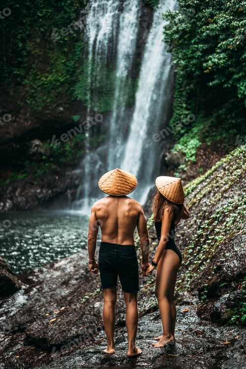 Preview: Couple admiring a beautiful waterfall in Indonesia. Tourists at the waterfall, rear view