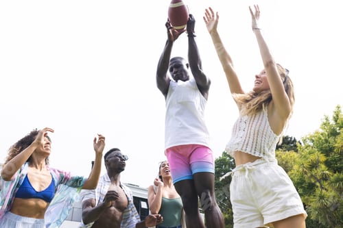 Preview: Young African American man catches a football, surrounded by friends in casual summer wear