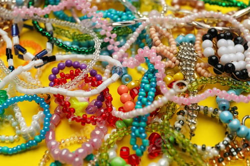Preview: Pile of beautiful handmade beaded jewelry on yellow background, closeup