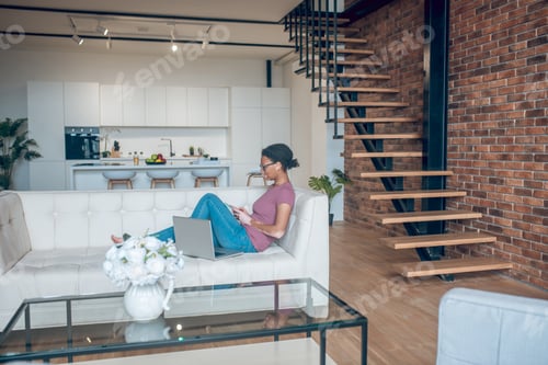 Aperçu: A woman in casual clothes surfing internet while resting at home