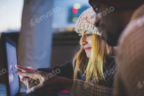 Preview: Couple using laptop outdoors at dusk