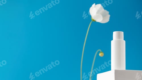 Preview: White tube with a cosmetic product on a podium on a blue background with a flower. Copy space