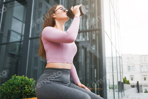 Preview: Young fitness woman with a beautiful figure drinks from a shaker