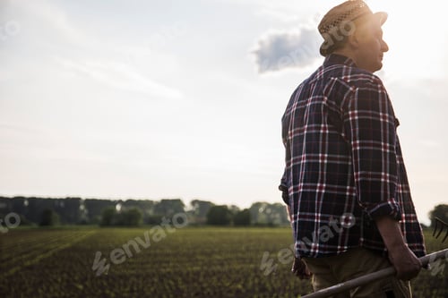Preview: Farmer holding rake next to a field