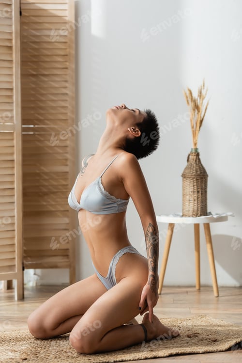 Preview: full length of young tattooed and passionate woman in lingerie sitting in seductive pose