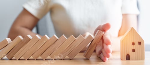 Preview: woman hand stop falling wood blocks and protect house model.