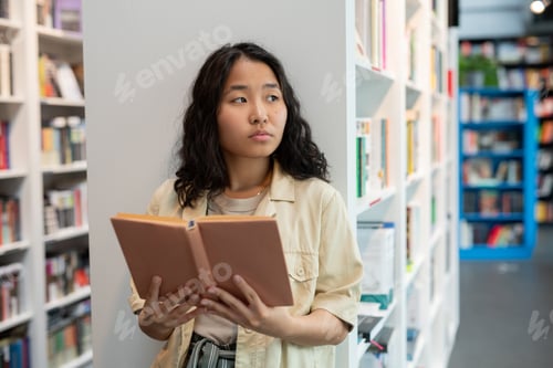 Preview: Young Asian woman holding open book in library