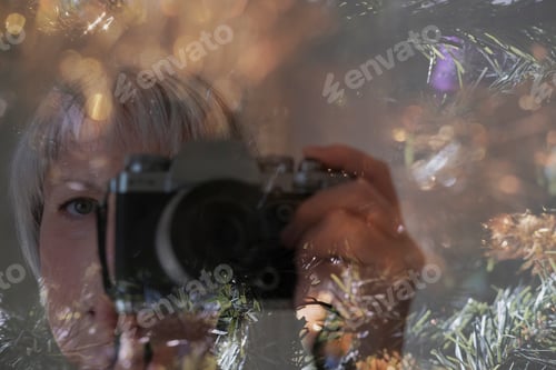 Preview: Mature woman takes self-portrait over of Christmas tree and blurred background.