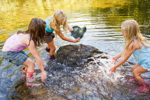 Preview: Children playing and pouring water from a bucket into a stream on a sunny day