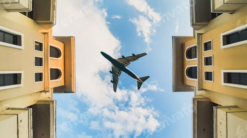 Preview: Aircraft flying over buildings under a cloudy blue sky