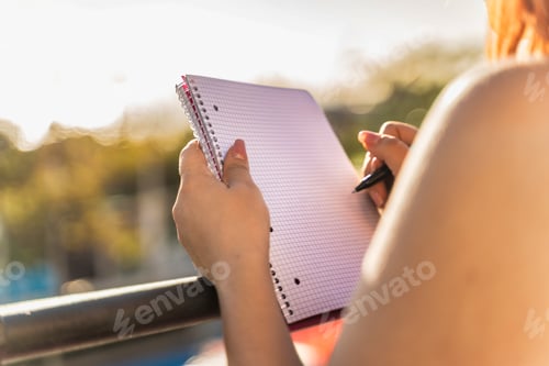 Preview: Woman Writing in Notebook Outdoors - Focused Study Session at Sunset