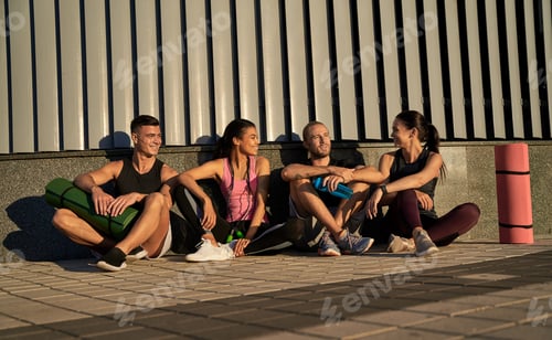 Preview: Happy four friends chatting after training outdoors