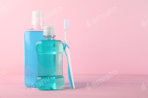 Preview: Mouthwash in bottles and toothbrush on pink background, space for text. Oral hygiene