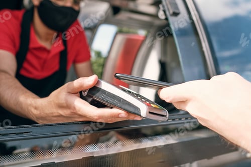 Preview: Seller of takeout food holding payment terminal while client paying for snack