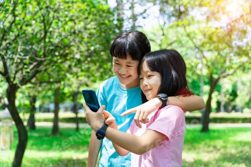 Preview: Two sisters hugging while using mobile phone in the park. Happy family concept.