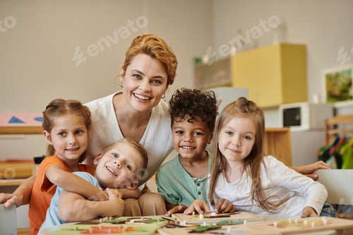 Preview: smiling teacher and multiethnic kids looking at camera during lesson in montessori school