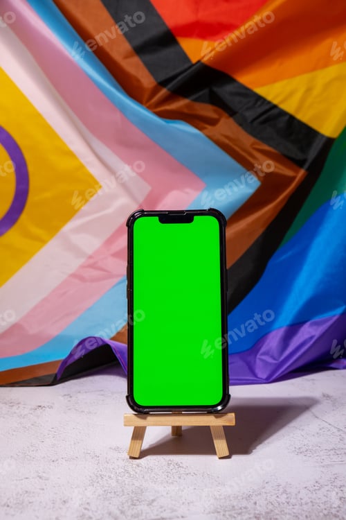 Preview: Mobile phone with chroma key on Rainbow LGBTQIA flag made from silk material background. Happy pride