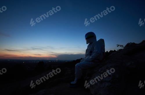 Preview: Astronaut sitting on rocky hill during sunset.