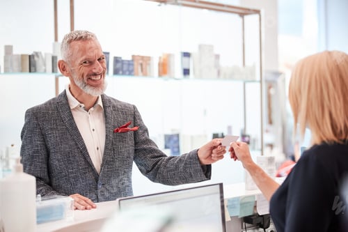 Preview: Contented man taking a card from a shop staffmember