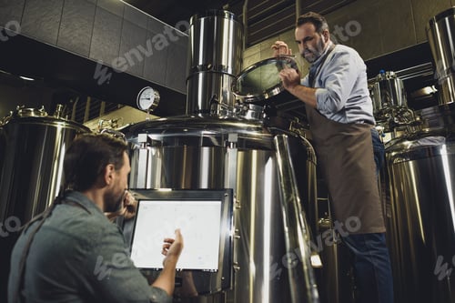 Preview: Male brewers in aprons working with tanks and industrial equipment at the brewery