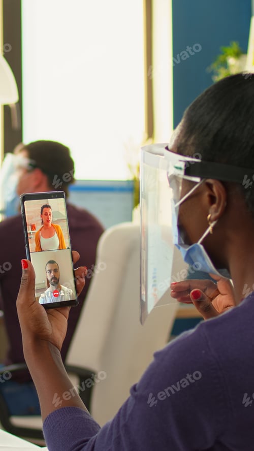 Preview: Black businesswoman with mask having videocall on smartphone