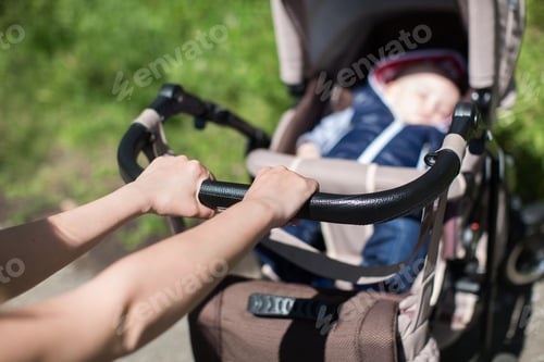 Preview: Young mother walking and pushing a stroller in the park