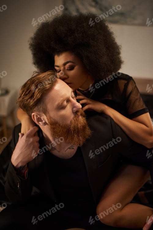 Preview: passionate night of multicultural couple at home, curly african american woman kissing tattooed man