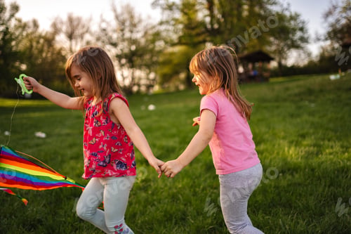 Preview: Sisters joyfully running together with a colorful kite in the park