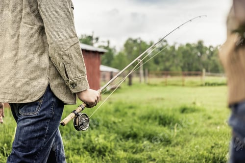 Preview: Cropped view of young mans mid section carrying fishing rod