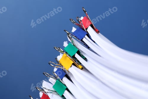 Preview: Binder clips with sheets of paper on blue background, closeup. Space for text