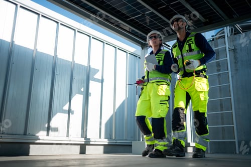 Preview: Male and female engineers inspecting photovoltaic systems beneath solar panel