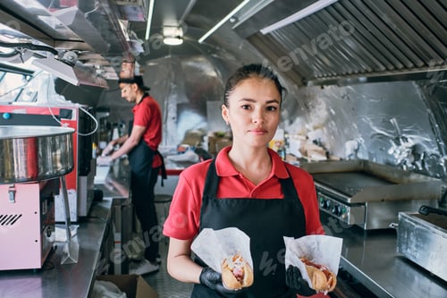 Preview: Young confident owner of street food truck holding hotdogs