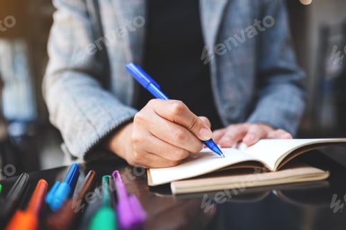 Preview: Closeup image of a woman writing on a blank notebook with colored pens on the table