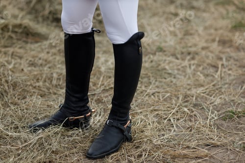 Preview: Female legs in black leather boots close up rider jockey standing at stable.