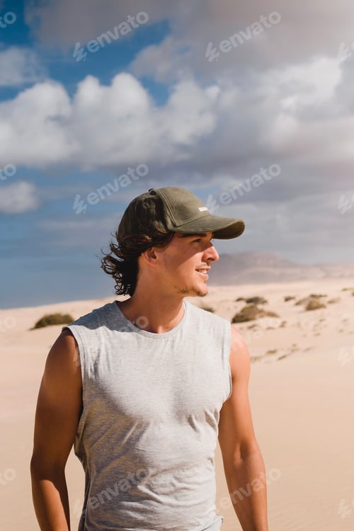Preview: Portrait photo of smiling young man with cap in the desert of the dunes of Fuerteventura