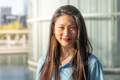 Preview: Portrait of a beautiful asian woman smiling and looking at camera outdoors during a sunny day.