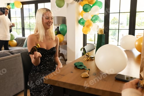 Preview: Blonde woman in black dress celebrating at home with balloons and party favors