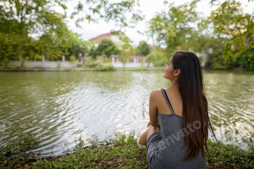 Preview: Young beautiful Asian woman relaxing by the lake at the park