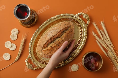 Preview: Bread on golden tray, hand, spikelets, grapes and cup of wine on orange background, top view