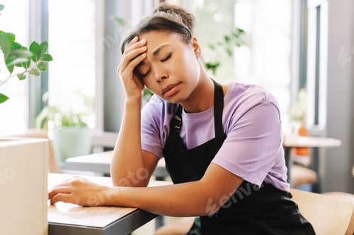 Preview: Tired african american waitress suffering headache sitting at table in cafe
