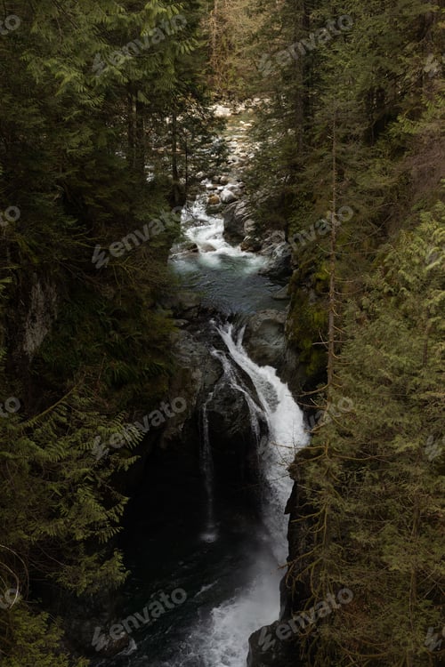 Preview: the large waterfall in the forest is surrounded by trees as it rains