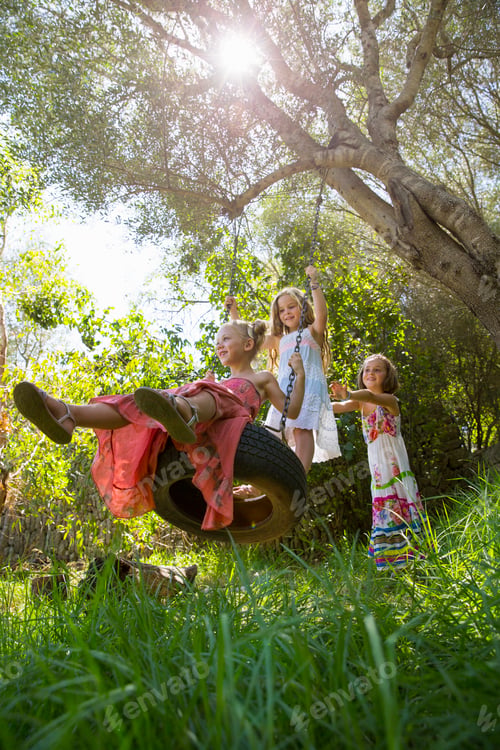Preview: Low angle view of three girls playing on tree tire swing in garden