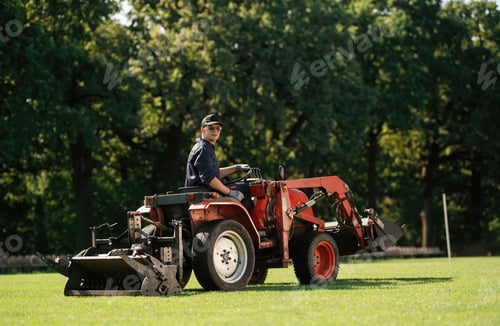Preview: Man is with utility tractor with grass cutter and aerator equipment on the field